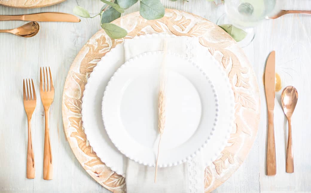A simple fall tablescape featuring a white and gold place setting adorned with eucalyptus leaves.