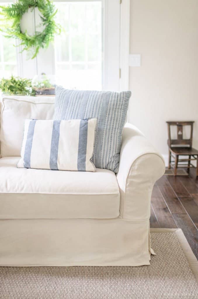 Pottery Barn Sofa Review — PB Comfort Slipcovered Sofa with blue throw pillows and greenery in the background