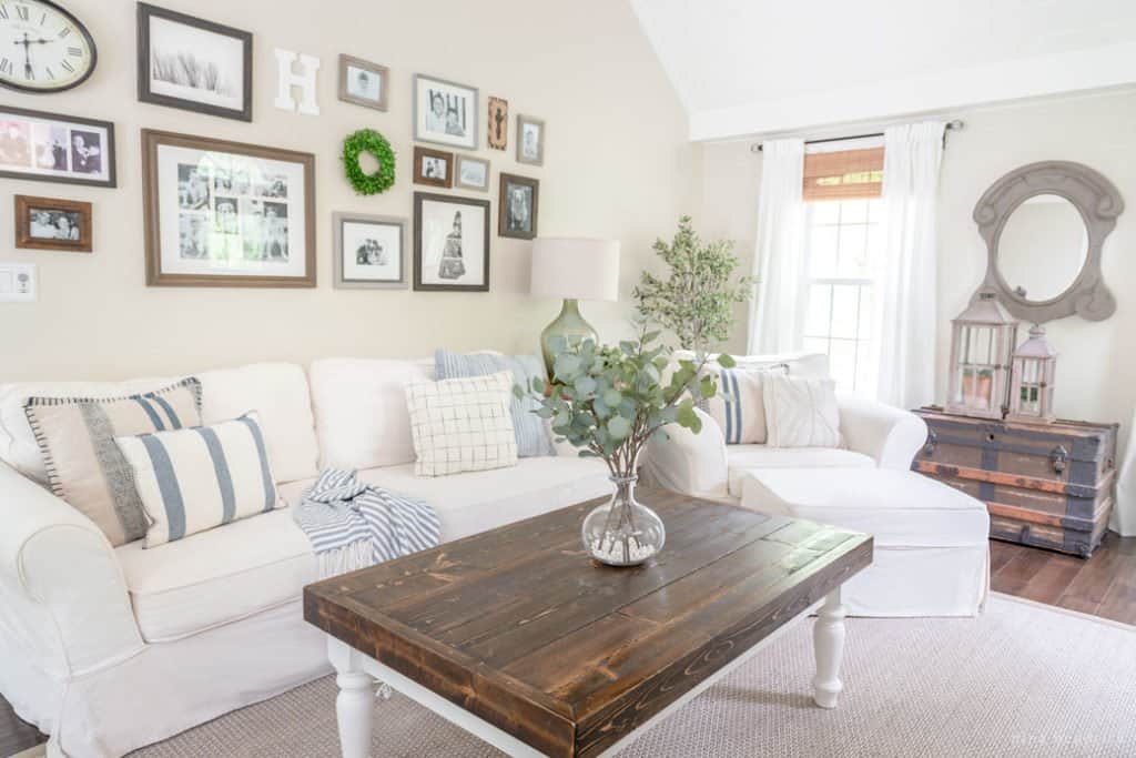 Family room with wood coffee table, white couches, and gallery wall of various wood stained picture frames. 