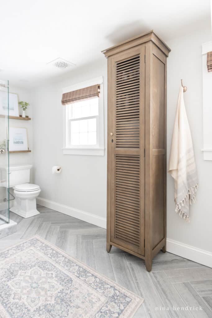 wood linen cabinet and a herringbone floor with a Ruggables rug