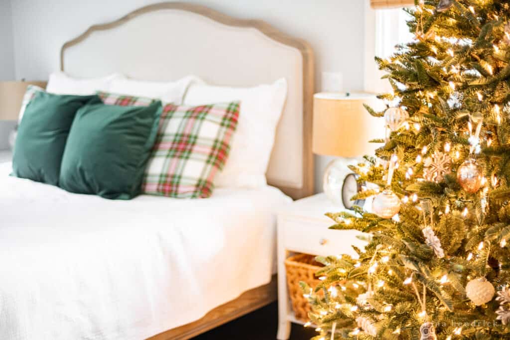 Christmas tree with rustic wood ornaments and a bed with throw pillows in the background.