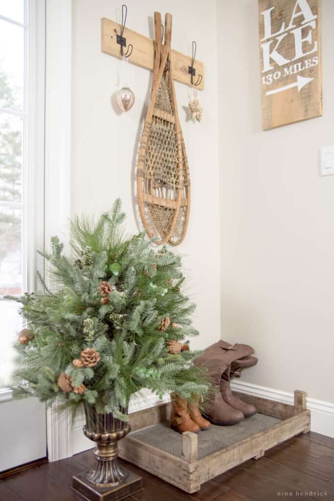 Evergreeen topiary Christmas decor with boots in a drying rack and vintage snowshoes hanging on a hook. 