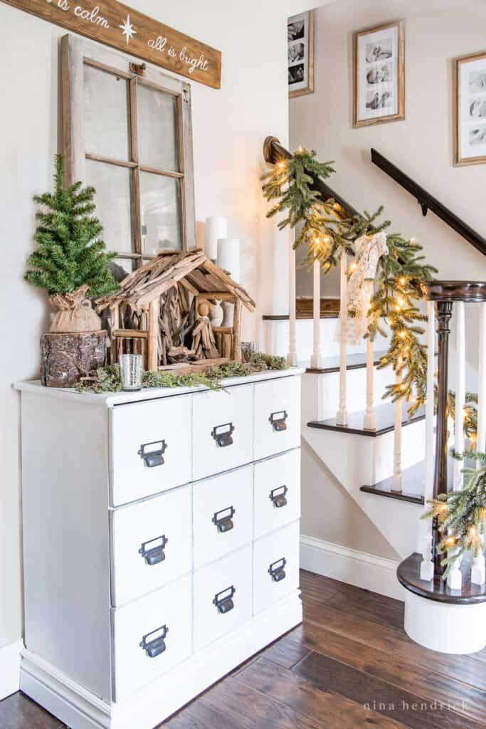 Rustic Christmas decorating ideas in the foyer — white dresser with driftwood nativity scene and evergreen garlands.