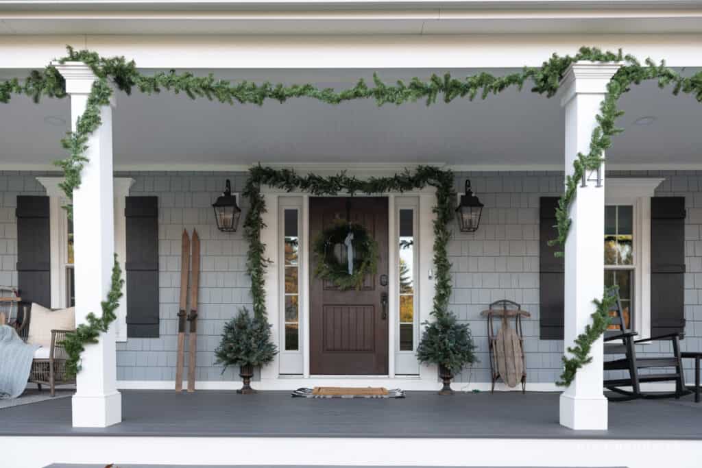 Front porch on a blue house with garland and a wreath with a blue ribbon