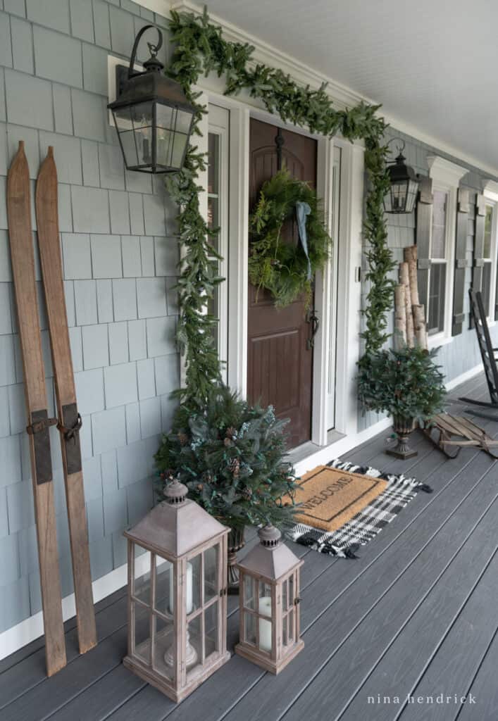 Front door surrounded by rustic Chrismas decorations and a wreath on the door with blue ribbon