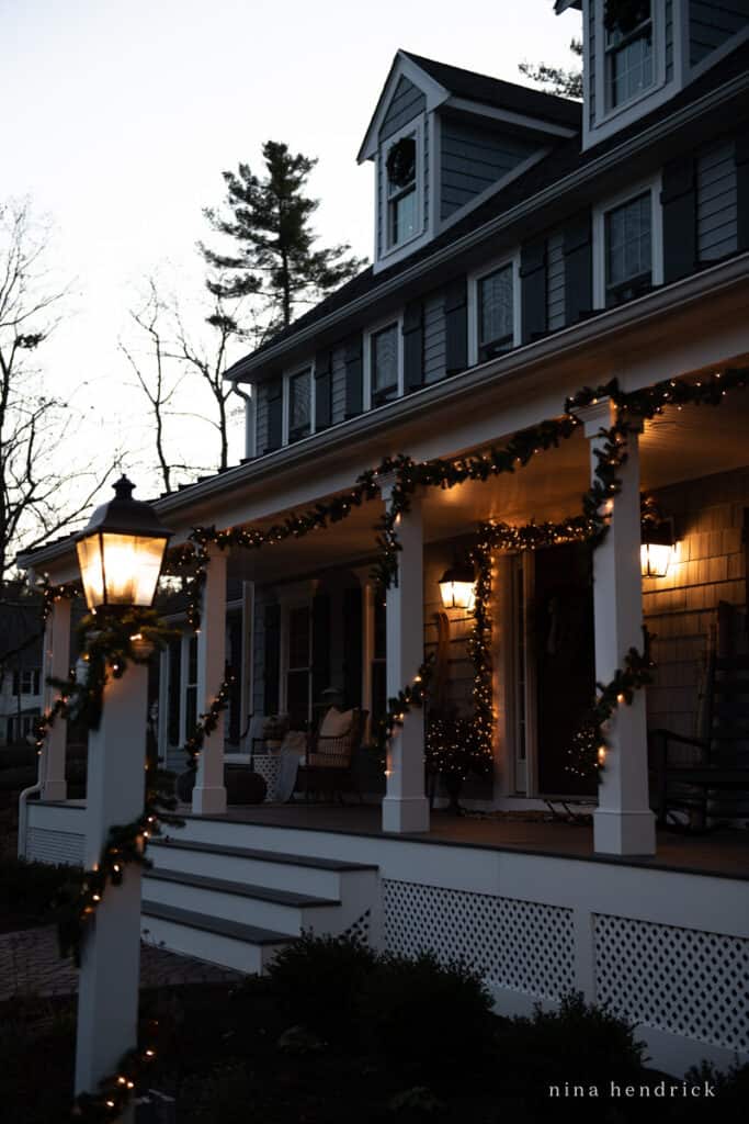 House at dusk with Christmas garlands wrapped around the posts and lanterns glowing