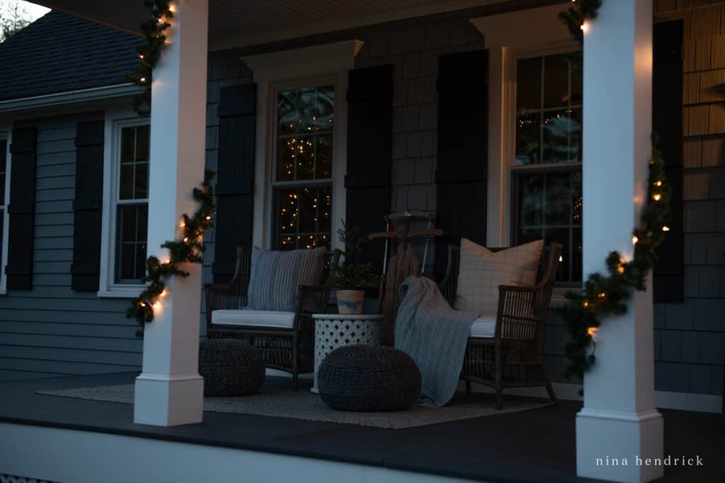 Porch with rattan chairs and posts wrapped in Christmas garland with a Christmas tree in the window