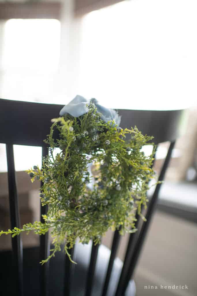 small juniper wreath on a black chair with a french blue ribbon