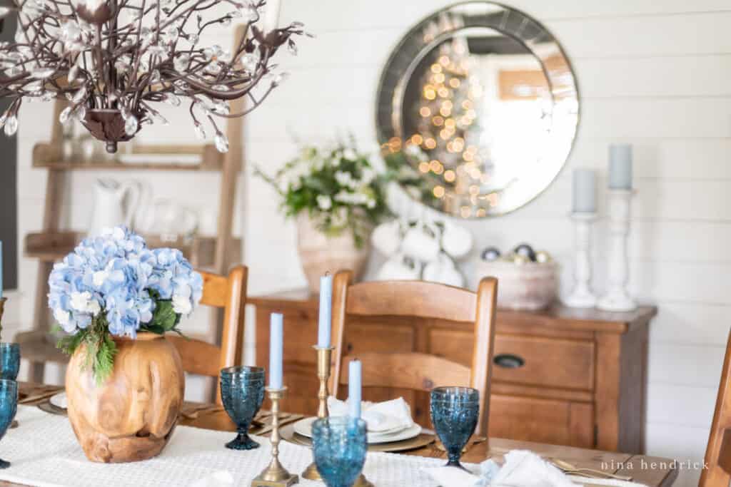 Hydrangeas in a wooden vase in a white dining room with a mirror in the background