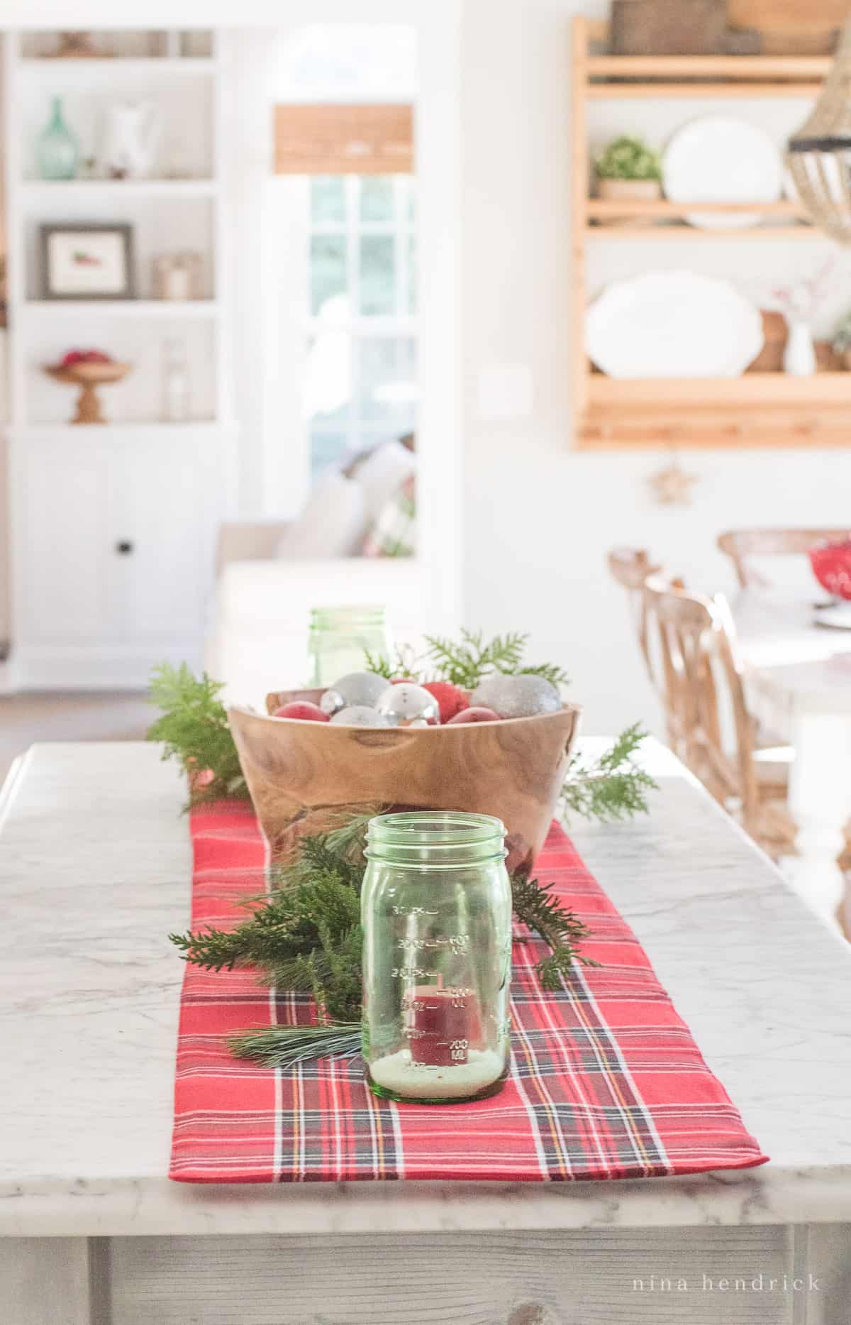 Kitchen countertop with simple Christmas decor — a mason jar with candle, evergreen clippings, and a bowl of ornaments