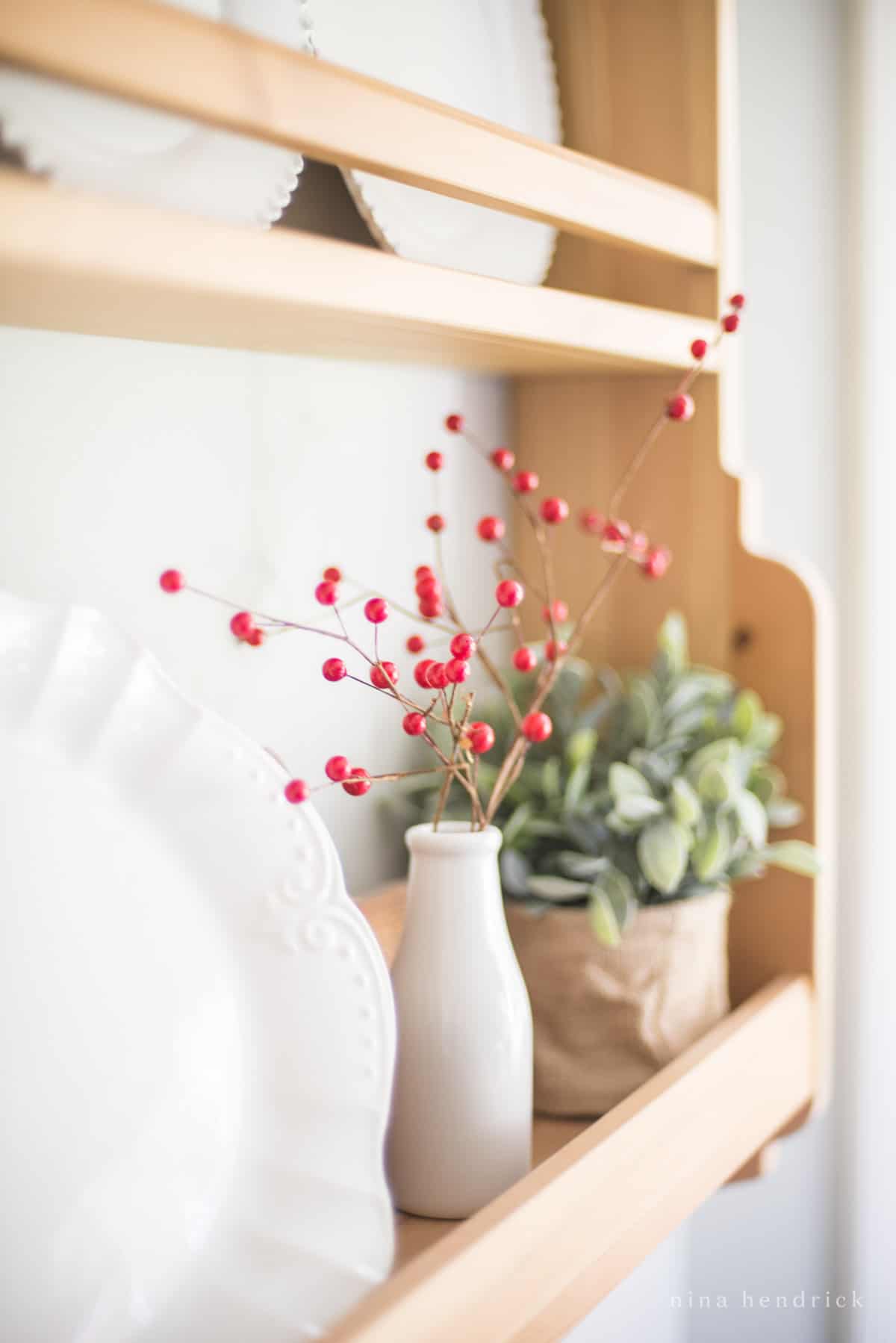 Red berries on a shelf with stark white plates and greenery