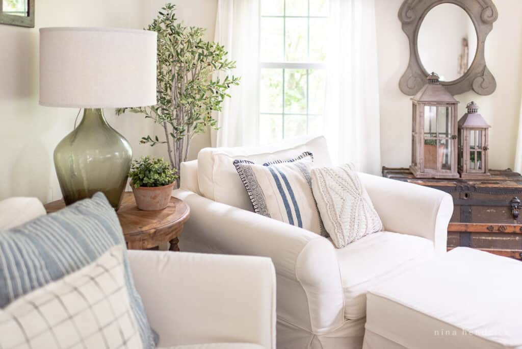 Oversized slipcovered armchair in the corner of a room with a green lamp and decor.