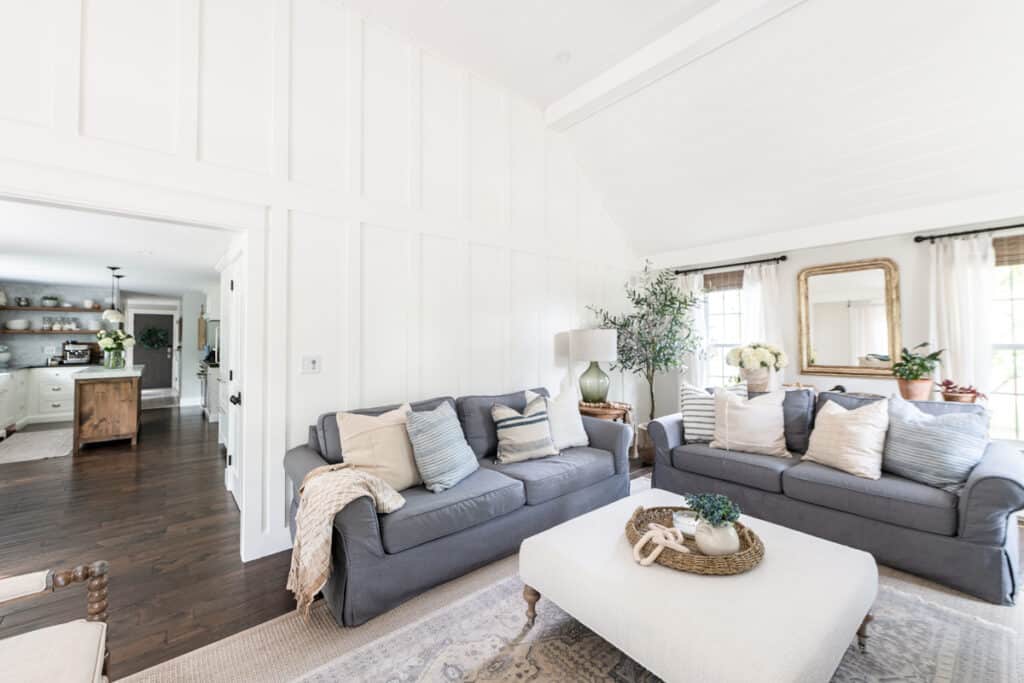 Two charcoal slipcovered sofas and an upholstered ottoman in a white board-and-batten family room.