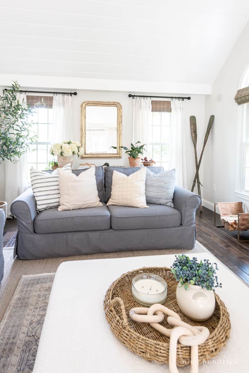 Charcoal slipcovered sofa in a white family room with decor and a gold mirror. 