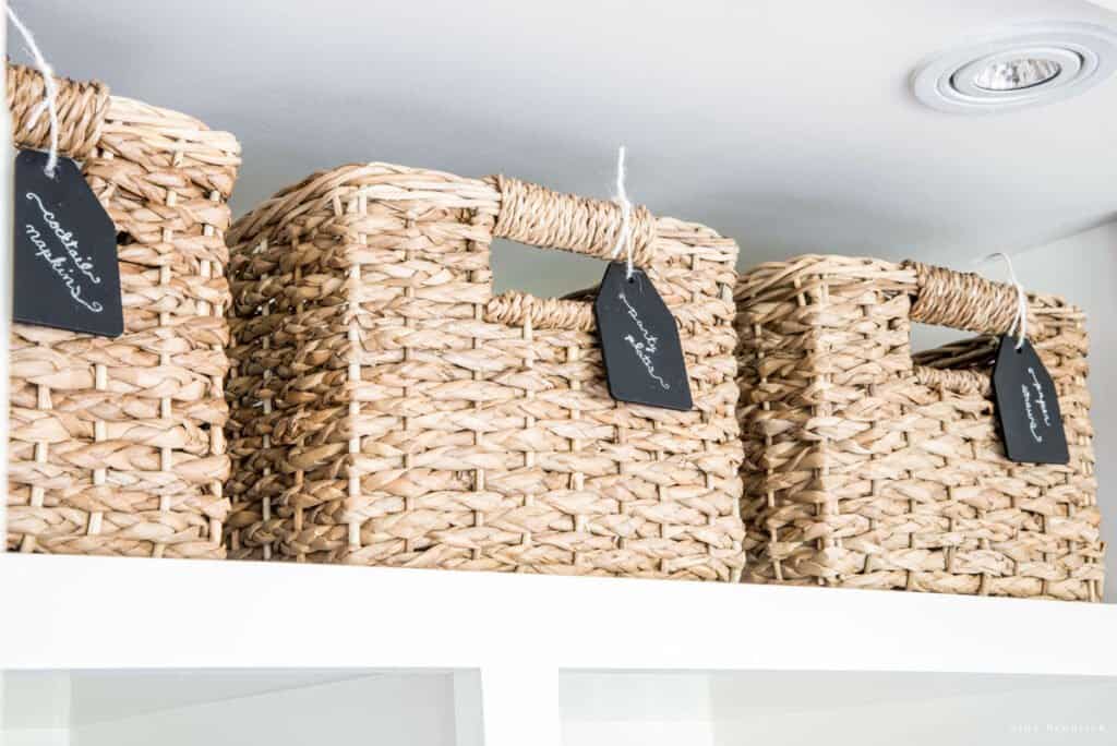 Items stored up high in wicker baskets with labels in a small pantry