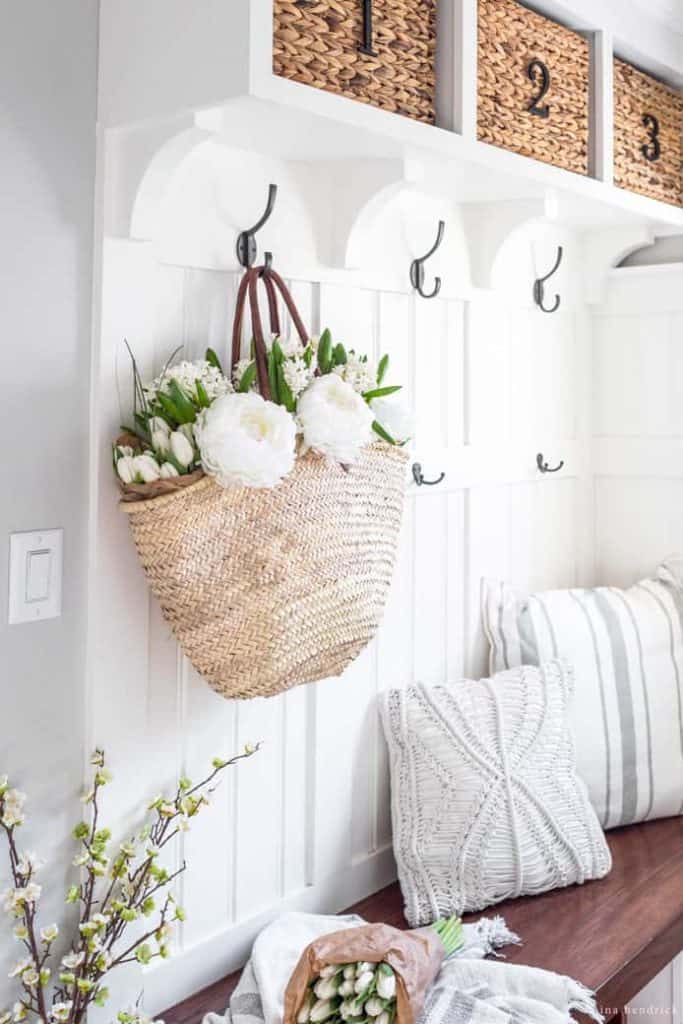 Spring Mudroom Decor | A fresh basket of flowers hangs in a mudroom decorated for Spring with throw pillows and branches. 