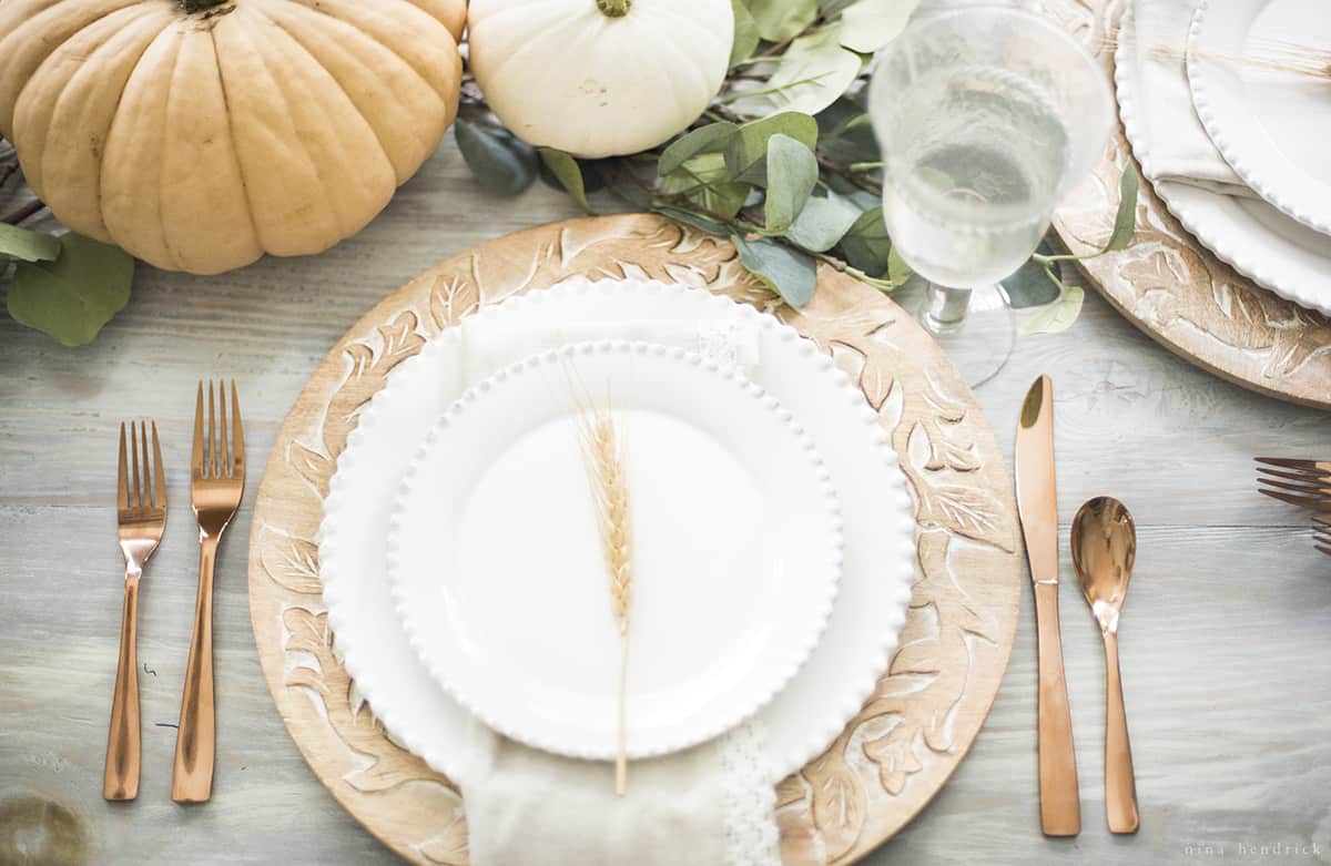 Thanksgiving place setting with white plates, silverware, and pumpkins.