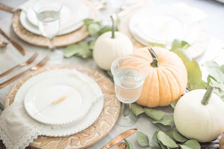 A white table setting with pumpkins and eucalyptus leaves.