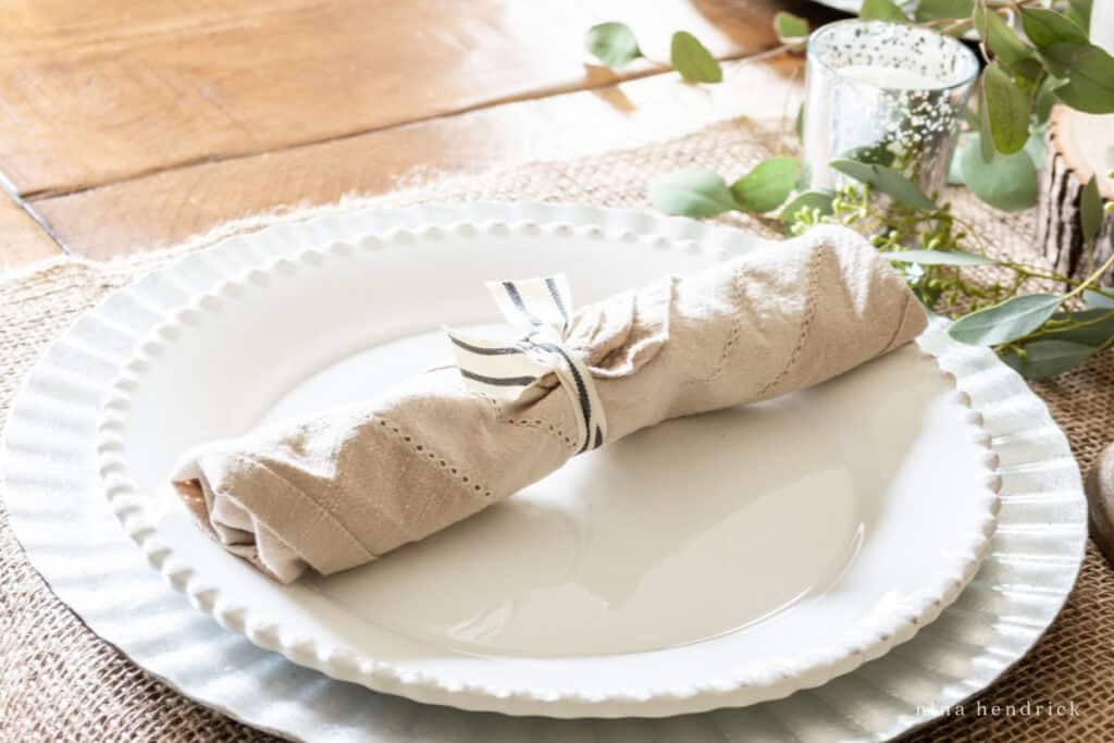 A white plate with a burlap napkin and eucalyptus leaves.