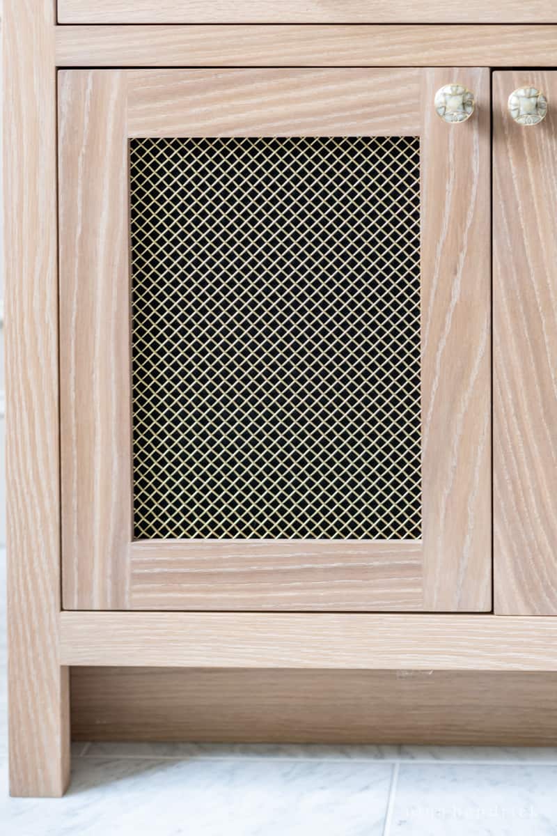 Brass mesh panel with black backing inset into a white oak bathroom vanity door