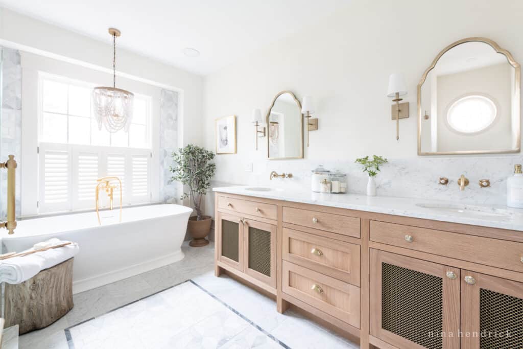 Bathroom remodel with warm white oak vanity, marble floor tiles, and a freestanding bathtub with brass tub filler