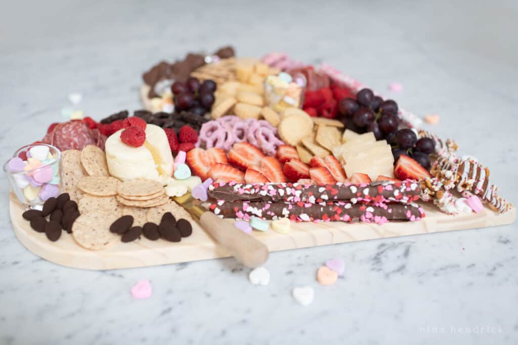 Heart-shaped Valentine's Day charcuterie board with crackers, cheese, pretzels, fruit, chocolate, and candy