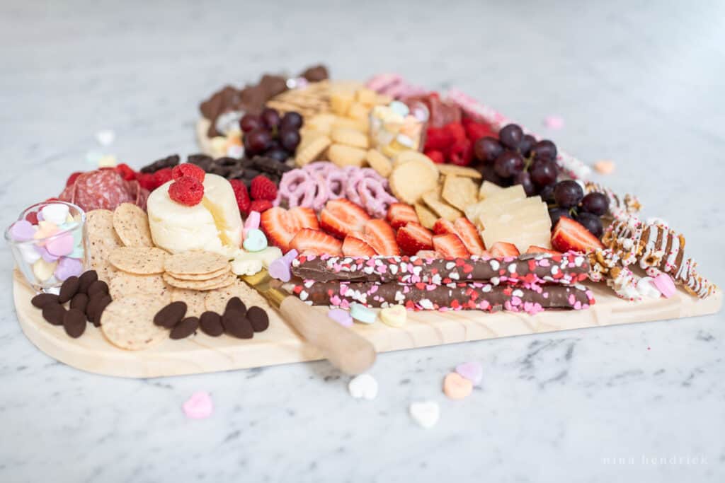 A festive, heart-shaped Valentine's Day Charcuterie board with chocolate, fruit, and cheese