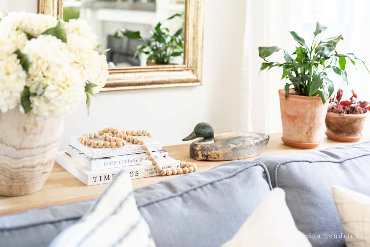 Vignette sofa table decor with a duck decoy, a stack of books, and a strand of wooden beads