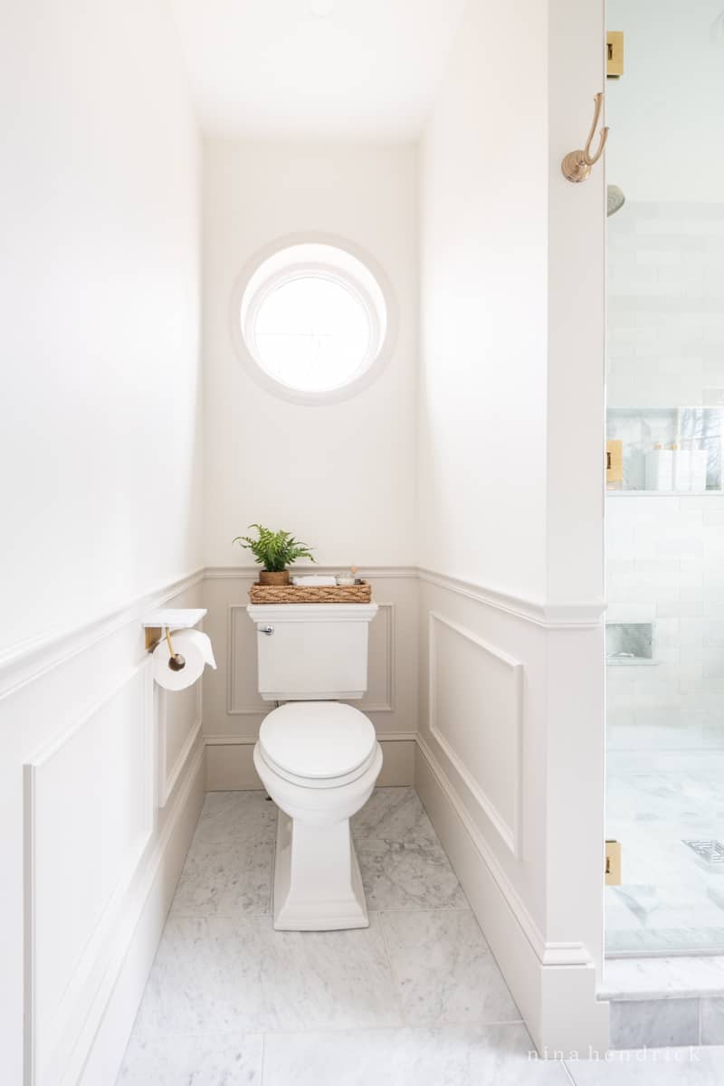 Timeless bathroom with a round window and picture frame wall molding