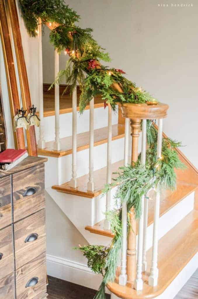 Christmas garland wrapped around a stair bannister next to a cozy Christmas vignette. 