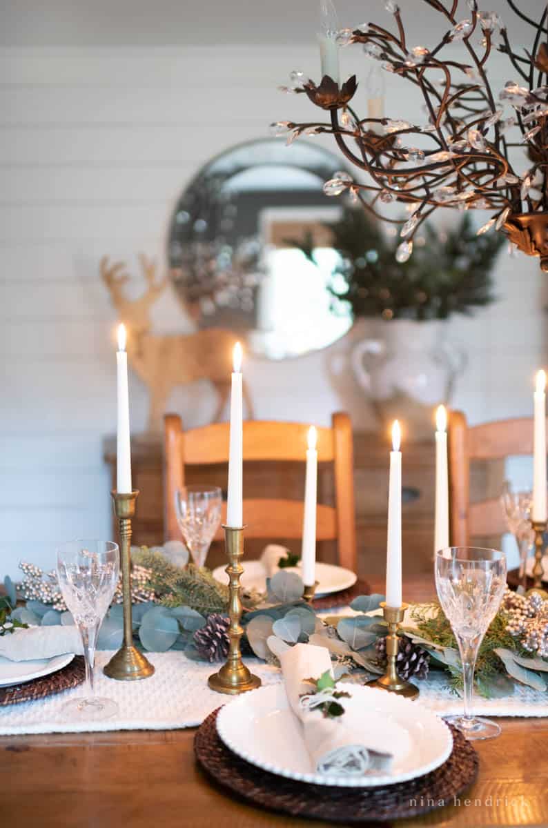 Winter centerpiece with evergreens and eucalyptus with brass candlesticks.