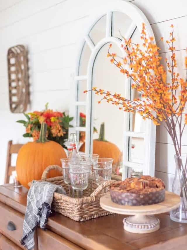 A dining room table with pumpkins, flowers and a mirror.