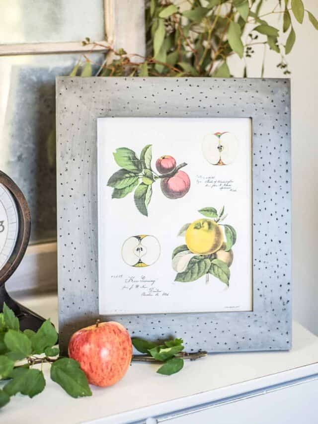 A framed print of apples and a clock on top of a dresser.