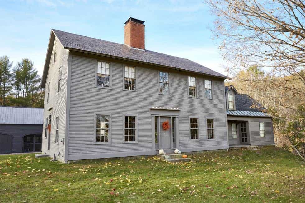 A New England style house with a chimney in the middle of a field.